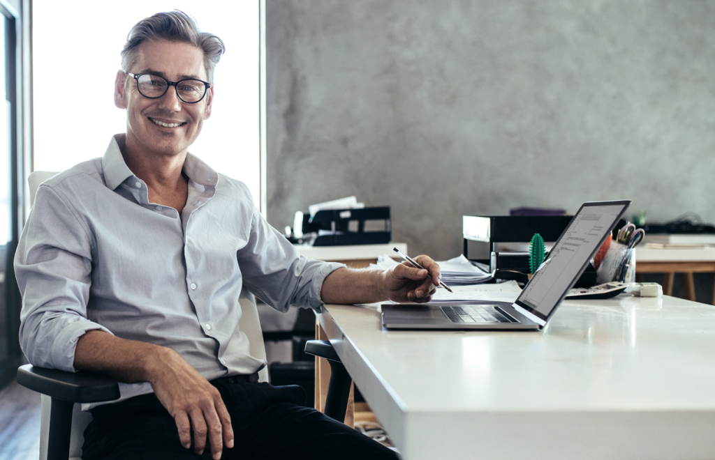 Man looking happy at his desk holding a pen. (Your Exiting ROBS Strategy 6-Step Guide - Guidant Financial Blog)